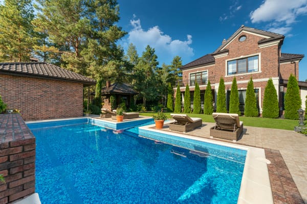 Elegant pool with manicured shrubs and brick home.